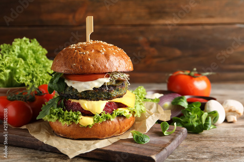Vegan burger and vegetables on table against wooden background