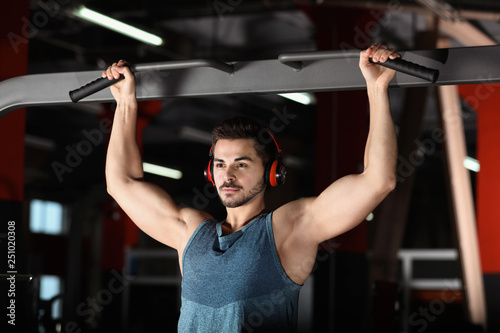 Young man with headphones listening to music and working out at gym