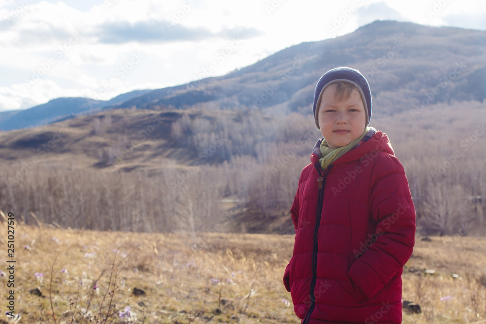 a contented six-year-old boy in a warm red jacket keeps his hands in his pockets outdoors a contented six-year-old boy in a warm red jacket keeps his hands in his pockets outdoors