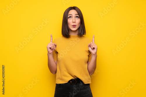 Young woman over yellow wall pointing up and surprised