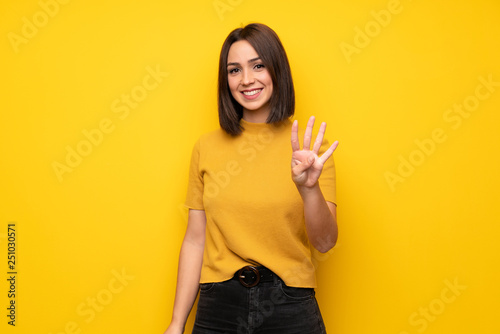 Young woman over yellow wall happy and counting four with fingers photo