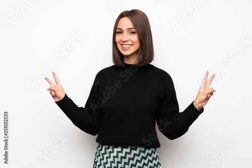 Young woman over white wall smiling and showing victory sign with both hands