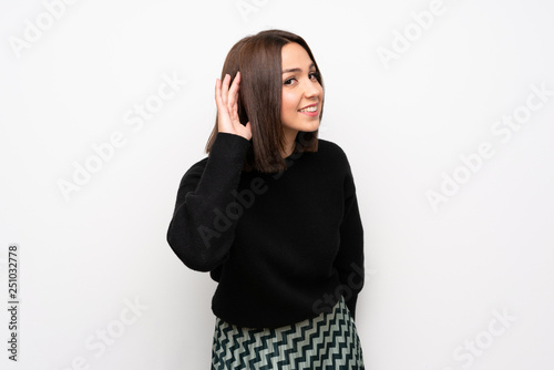 Young woman over white wall listening to something by putting hand on the ear