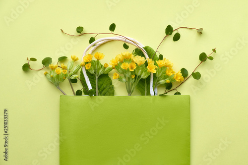 Yellow primrose flowers in a green shopping bag with space for text on yellow paper