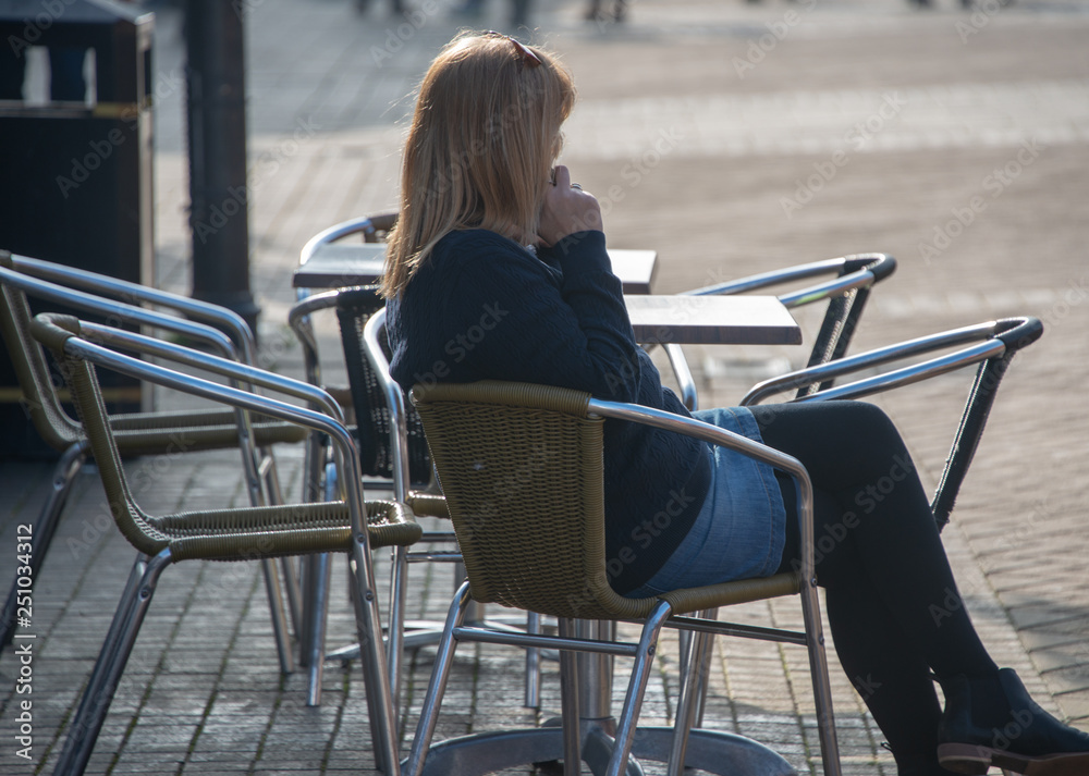 woman using mobile phone whilst sat alone outside cafe in street woman using mobile phone whilst sat alone outside cafe in street
