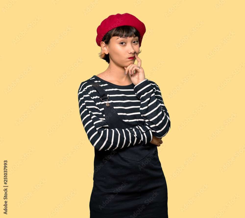 Young woman with beret thinking over yellow background