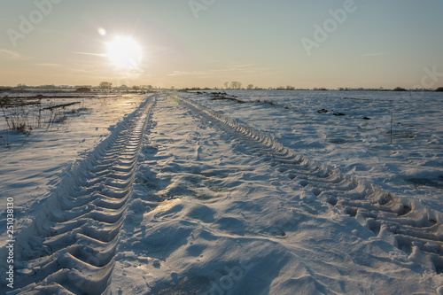 Vehicle tire tracks on snow and sun over the horizon