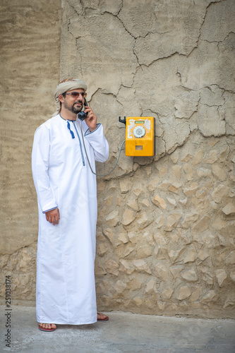 Arab Man talking on old fasioned public phone in Al Seef area of Dubai photo