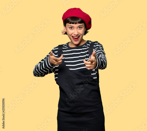 Young woman with beret points finger at you while smiling