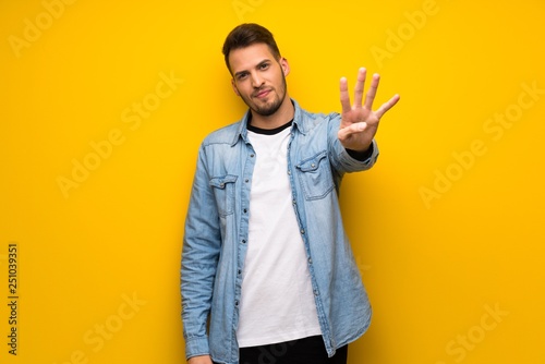 Handsome man over yellow wall happy and counting four with fingers