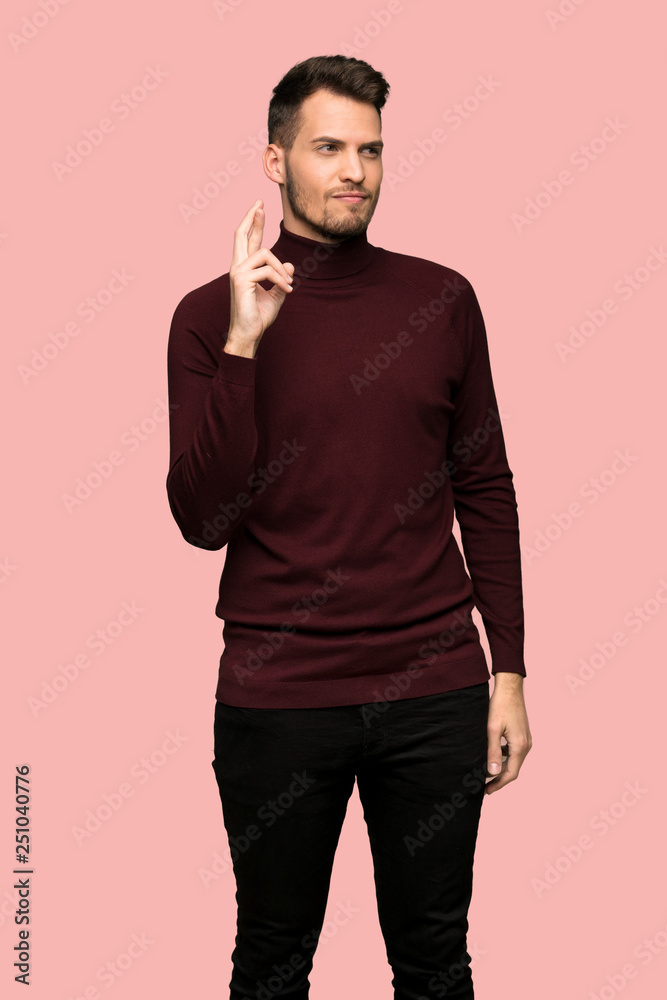 Man with turtleneck sweater with fingers crossing and wishing the best over pink background Man with turtleneck sweater with fingers crossing and wishing the best over pink background