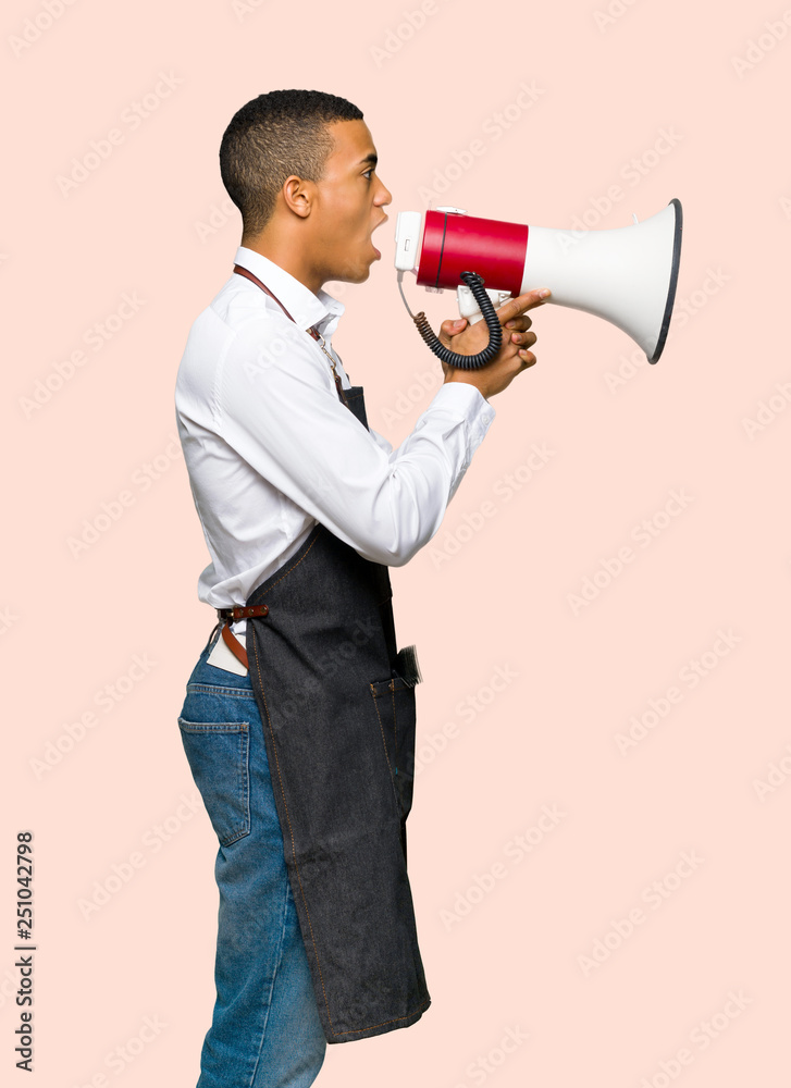 Young afro american barber man shouting through a megaphone to announce something in lateral position on isolated background Young afro american barber man shouting through a megaphone to announce something in lateral position on isolated background