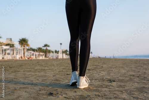Bottom view of woman legs in the sport leggings and sneakers on the beach at the morning, healthy lifestyle.