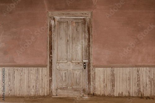 Photography Closed wooden door against pinkish orange wall with wainscoting in an abandoned