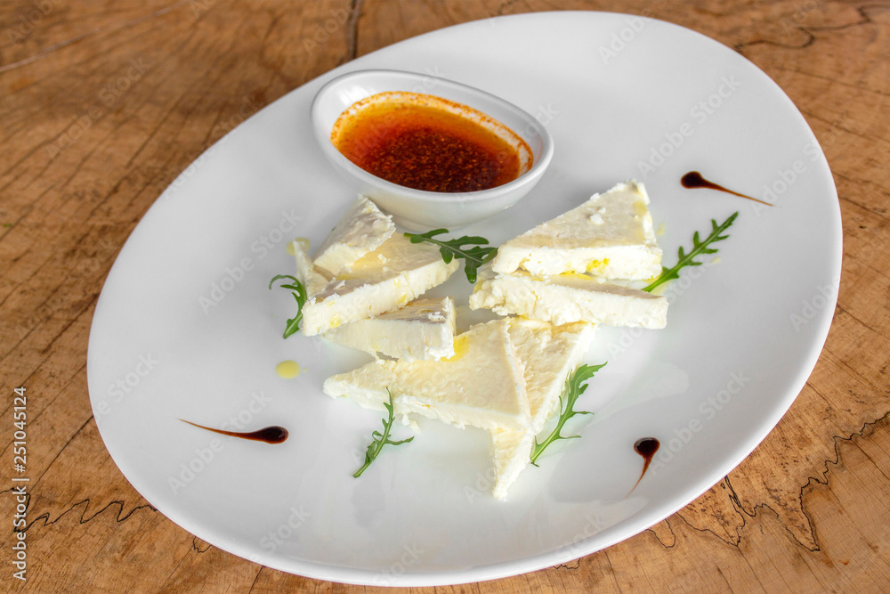 White cheese typical of the Balkans with arugula, dressing and, optionally, olive oil with red pepper. In a white plate on a wooden background. White cheese typical of the Balkans with arugula, dressing and, optionally, olive oil with red pepper. In a white plate on a wooden background.