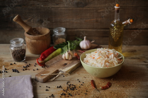sauerkraut in a bowl on a wooden table with oil in a bottle, spices and herbs
