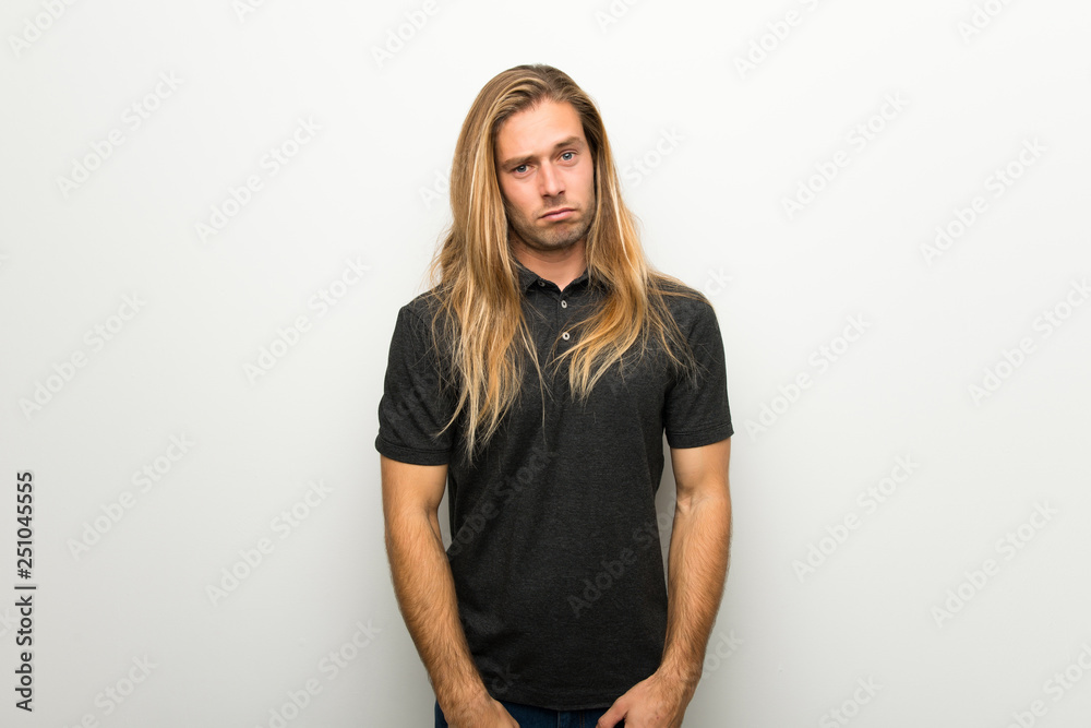 Blond man with long hair over white wall with sad and depressed expression Blond man with long hair over white wall with sad and depressed expression