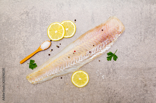 Fresh raw hake fillet on a stone background. With lemon, parsley, salt in wooden spoon and peppers mix. Top view