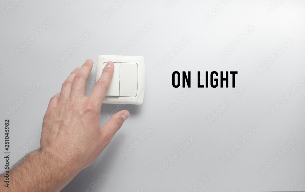 Hand presses a light switch on gray wall background. On light. Hand presses a light switch on gray wall background. On light.
