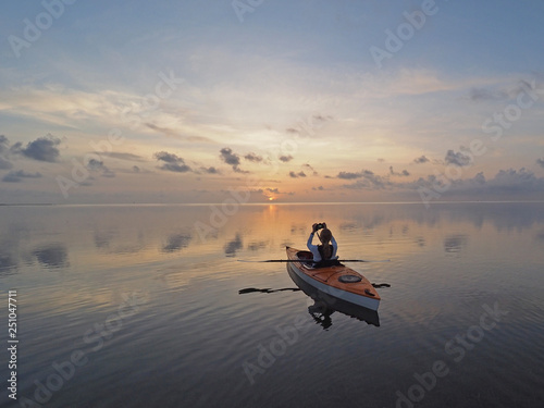 Woman kayaking at sunrise on the perfectly still water of Bear Cut off Key Biscayne, Florida.