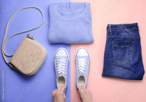 Women's accessories, clothing shoes on a pastel background. Jeans, sweater, bag. Women's hands hold sneakers. Creative flat lay. Top view. minimalism .