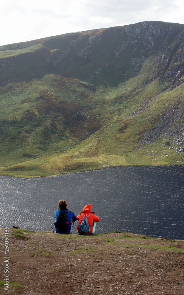 A couple of tourists sitting over a mountain lake. 