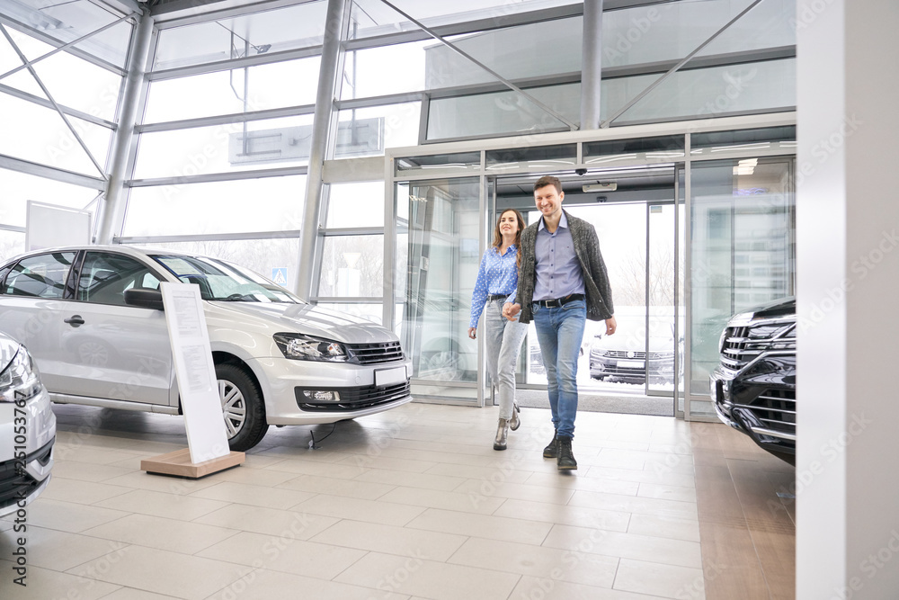 Fototapeta premium Couple entering dealership showroom, holding hands.