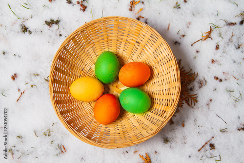 Five colorful easter eggs in a straw basket on top of snow and grass isolated egg hunt