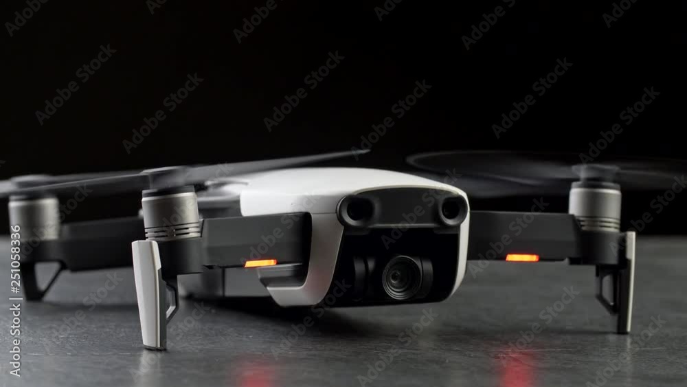 Compact drone quadcopter with digital camera, engines on. Over black background. 4K UHD