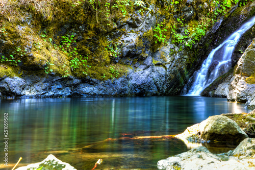 Schilderij op canvas Gentle waterfall pours into a clean clear pool of water close to a hiking trail