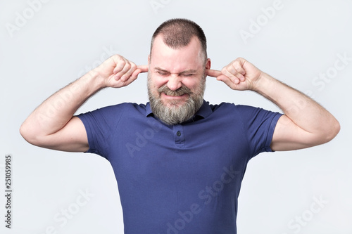 Obraz na płótnie Senior man, covering closed ears annoyed by loud noise not wanting to hear story