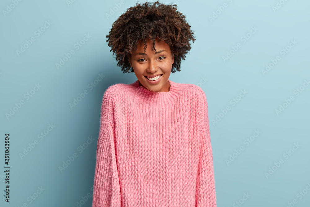 Happy joyful woman with pleased expression, expresses good emotions, wears pink sweater, isolated over blue background. Optimistic lady being in high spirit, satisfied to recieve compliment. Happy joyful woman with pleased expression, expresses good emotions, wears pink sweater, isolated over blue background. Optimistic lady being in high spirit, satisfied to recieve compliment.