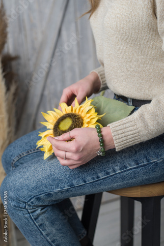 the girl is sitting on a chair and holding a sunflower, the girl has a jade bracelet, the girl is holding an artificial sunflower flower (vertically). photo