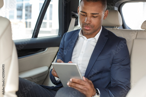 Young businessman sitting on back seat in car browsing digital tablet concentrated © Viktoriia