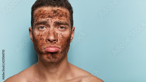 Photo of attractive man uses anti age coffee scrub, poses shirtless, purses lips, has spa treatments, isolated over blue background with blank space for your promotional content. Cosmetology