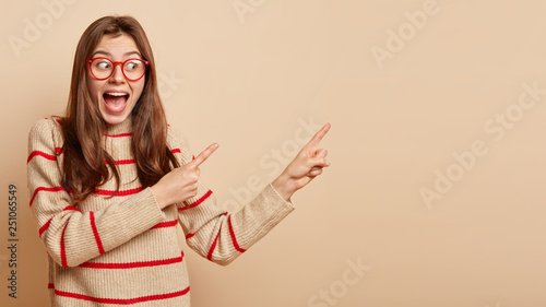 Cuadro en lienzo Studio shot of amazed overjoyed young female model opens mouth widely, demonstra