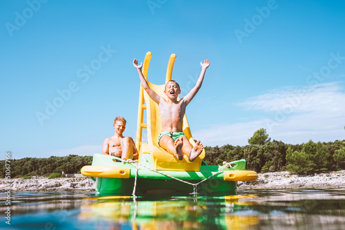 Little boy sliding down into sea water from floating Playground slide Catamaran as she enjoying sea trip with his brother © Soloviova Liudmyla