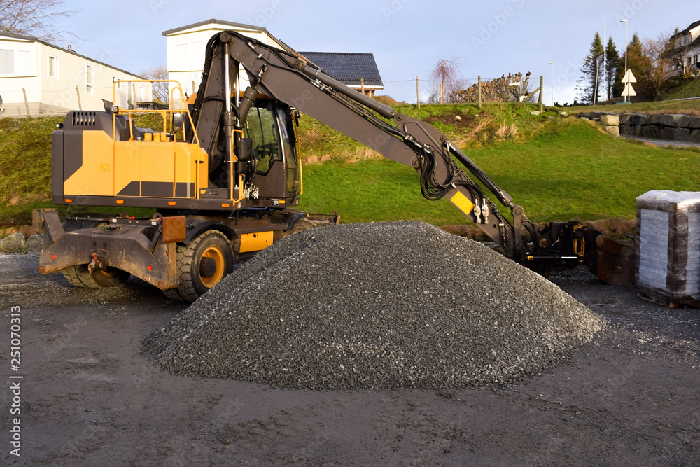 A large excavator stands on an asphalt site. A pile of fine rubble and an excavator. A large excavator stands on an asphalt site. A pile of fine rubble and an excavator.
