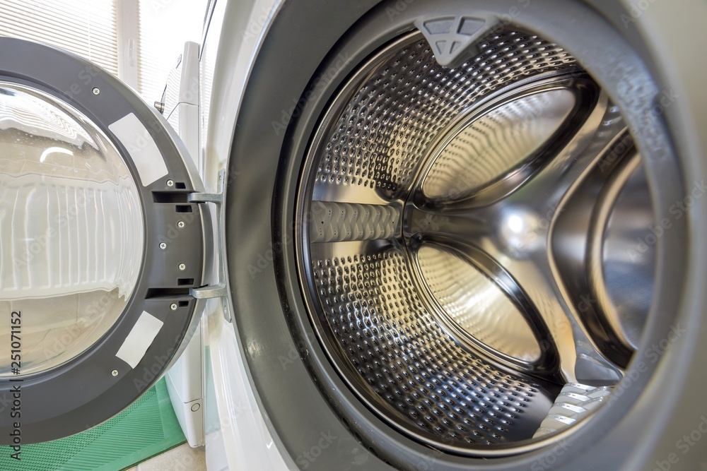 Close-up detail of modern washing machine interior with open door interior. Silver shiny stainless drum, design and technology.