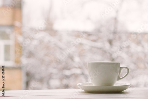 White cup in window sill on a background of house and snowy weather.