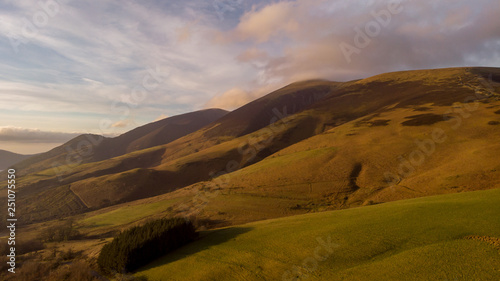 Mountain view with grassy slope, blue sky, sunny light, white cloud and trees