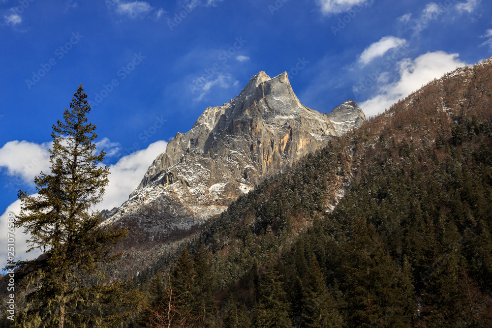 Siguniangshan - Four Girls Mountain National Park in Sichuan Province, China. ShuangQiao Valley Scenic Area, Snow Capped Jagged Mountains with clouds forming at the summit. Blue Sky, Snow Mountains