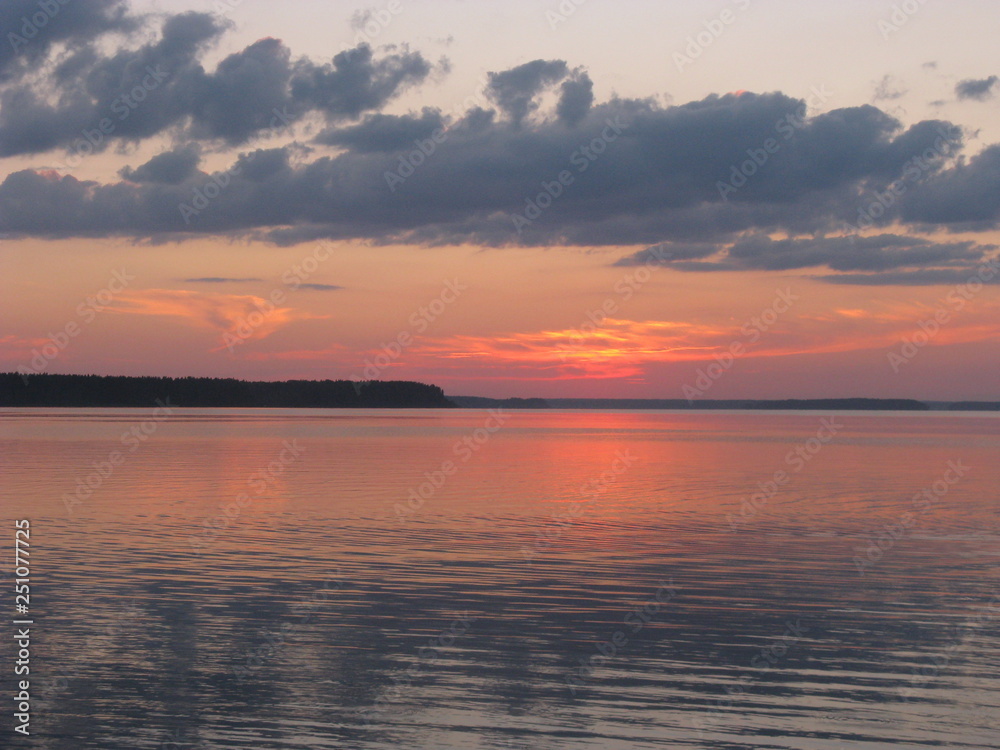 puesta del sol con nubes gris y cielo rosado, sobre lago 
