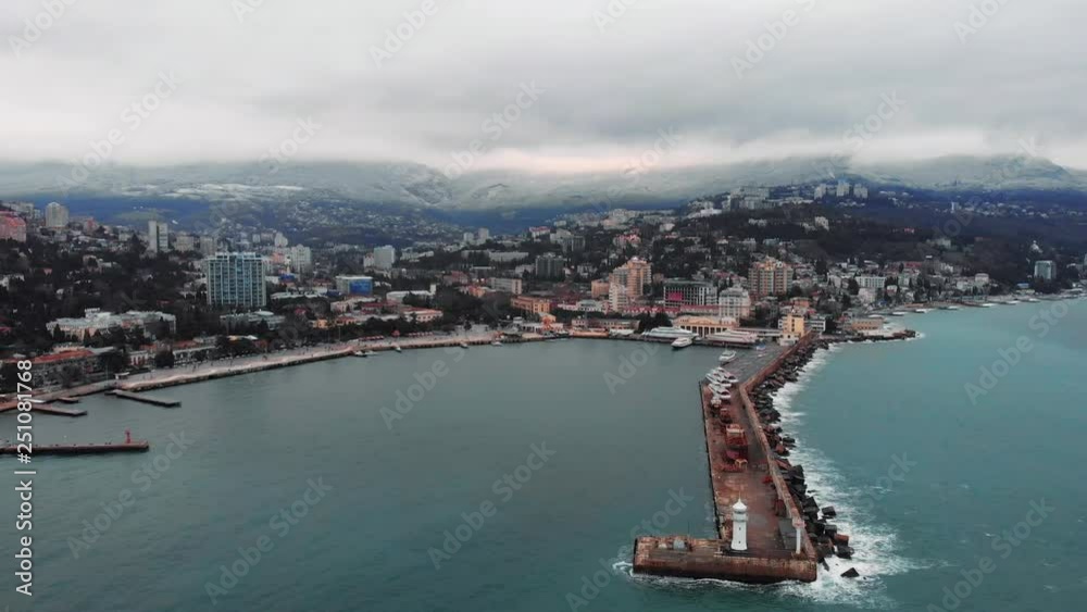 Aerial view of Yalta embankment from drone, old Lighthouse on pier, sea coast landscape and city buildings on mountains, beautiful winter panorama of European resort, Crimea. Aerial view of Yalta embankment from drone, old Lighthouse on pier, sea coast landscape and city buildings on mountains, beautiful winter panorama of European resort, Crimea.