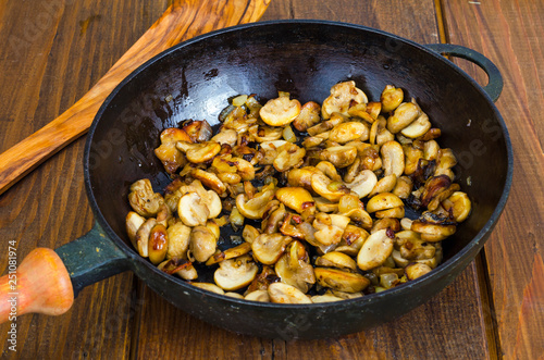 Black cast iron pan with fried mushroom slices on wooden background.