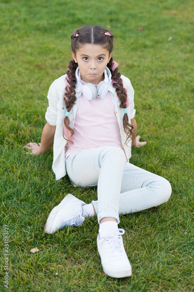 What makes child happy. Girl braids hairstyle and modern headphones enjoy relax. Secrets to raising happy child. Girl cute kid green grass background. Healthy emotional happy kid relaxing outdoors What makes child happy. Girl braids hairstyle and modern headphones enjoy relax. Secrets to raising happy child. Girl cute kid green grass background. Healthy emotional happy kid relaxing outdoors