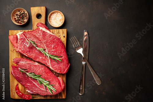 raw New York steaks with ingredients on a chopping board. on the background of dark stone. with copy space