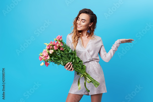 Young happy smiling redhead woman holding bouquet of colorful spring flowers isolated on blue background. Pink roses, festive bouquet in honor of women's day on March 8 or birthday