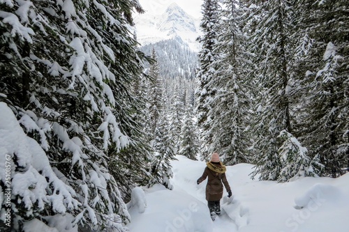 A young woman snowshoeing through forests of Island Lake in Fernie, British Columbia, Canada. The majestic winter background is an absolutely beautiful place to go snowshoeing with fresh fallen snow.