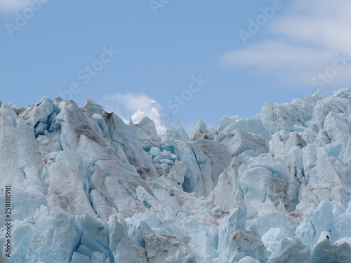 Looking up a the jutting edges of blue icebergs against a blue sky